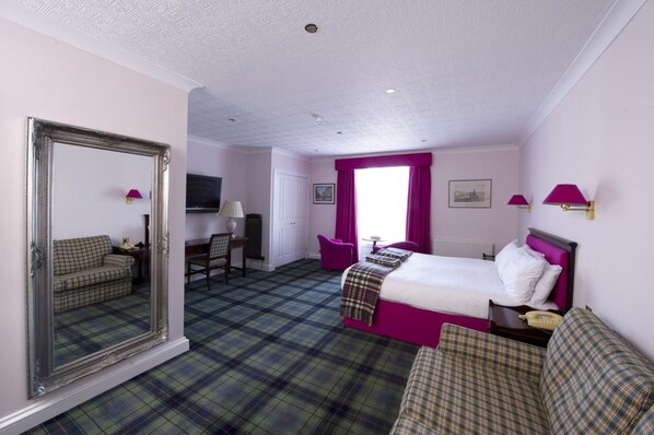 A hotel room with a bed, a chair, a desk, a mirror, and a window with curtains.