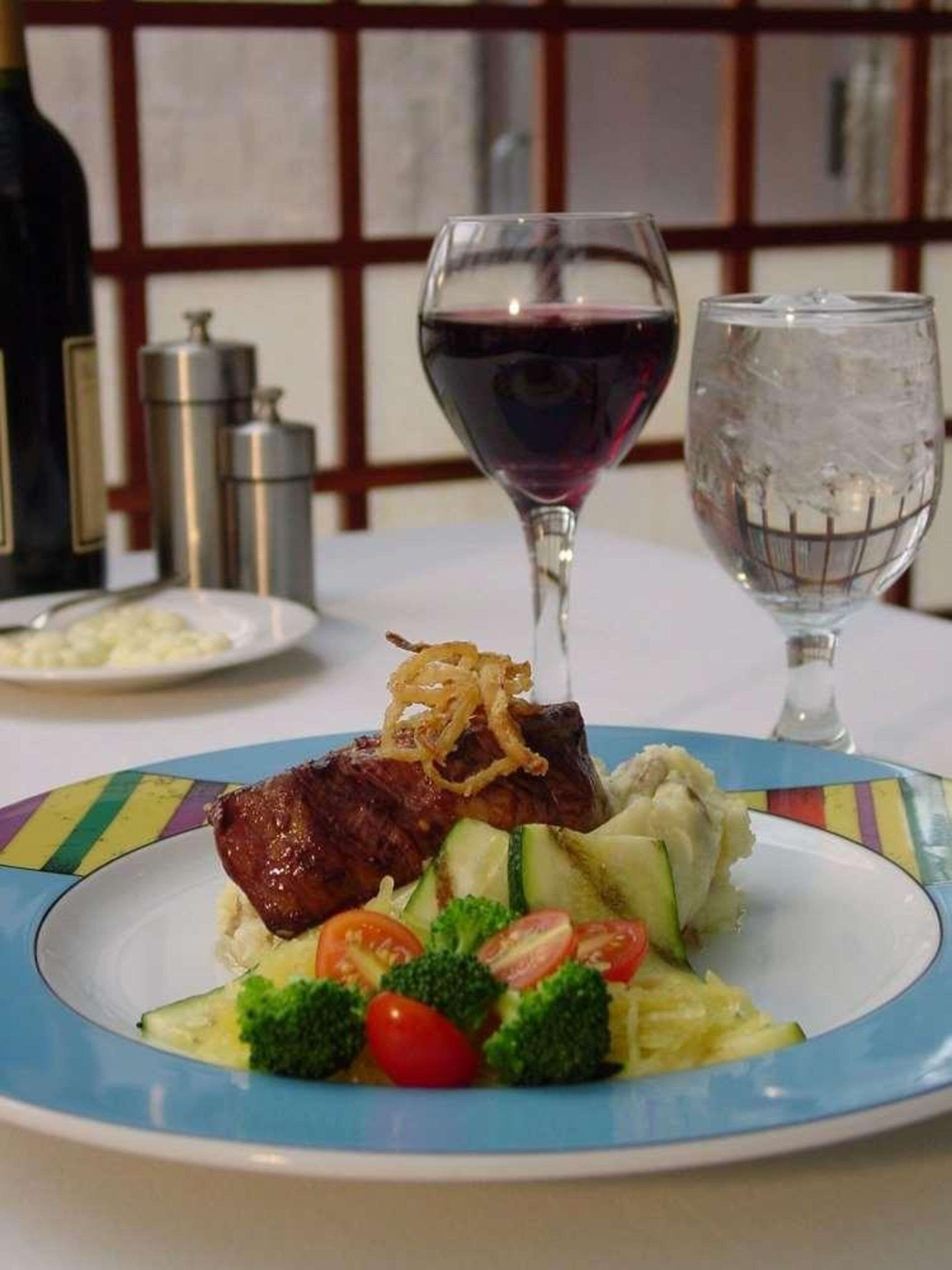 A plate of food with a glass of red wine and a glass of water on a table.
