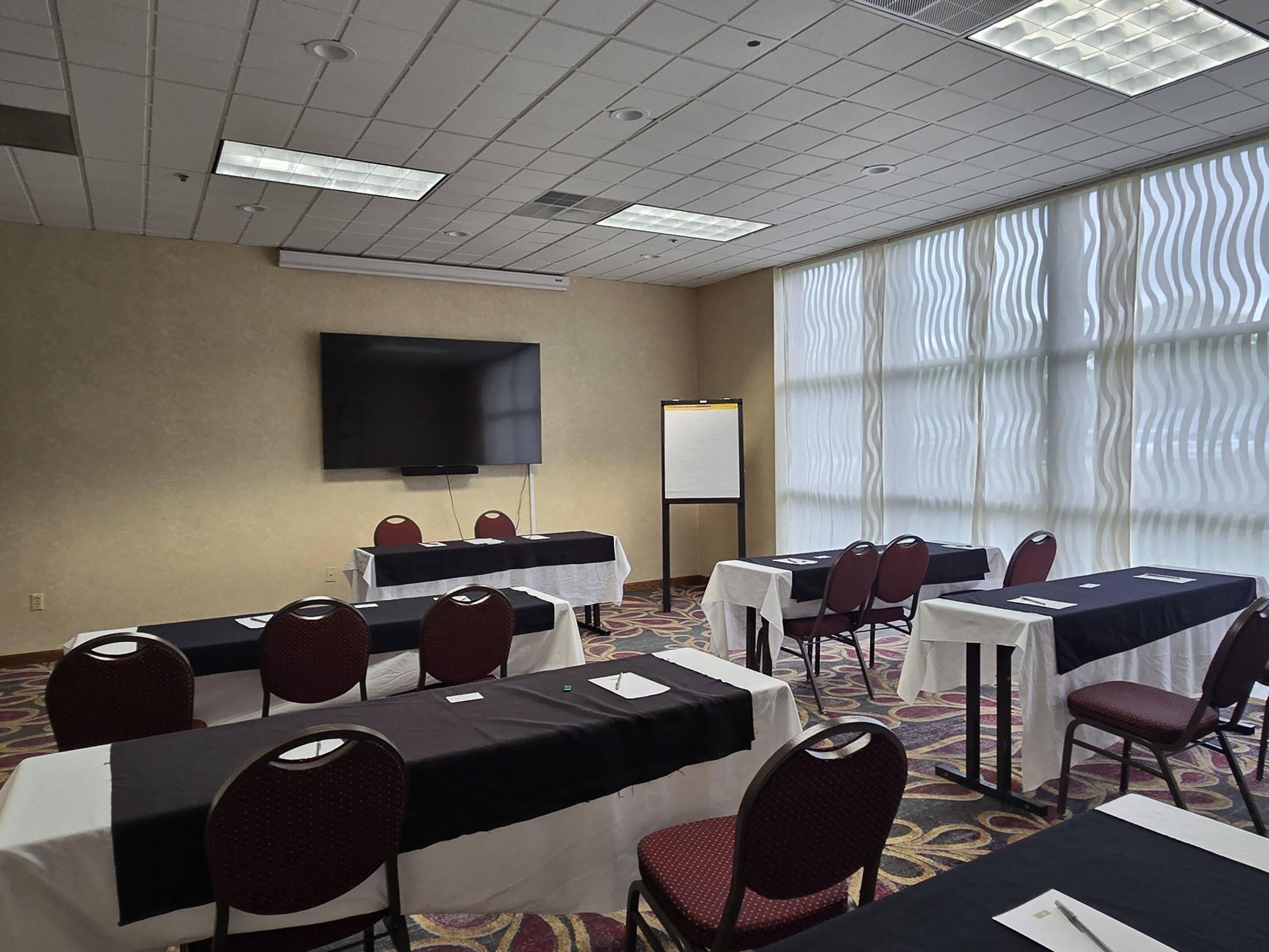 A conference room with tables, chairs, a TV, and a whiteboard.