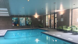 An indoor swimming pool with clear water, surrounded by lounge chairs and artwork on the walls. - Radisson Hotel Corning (Corning)