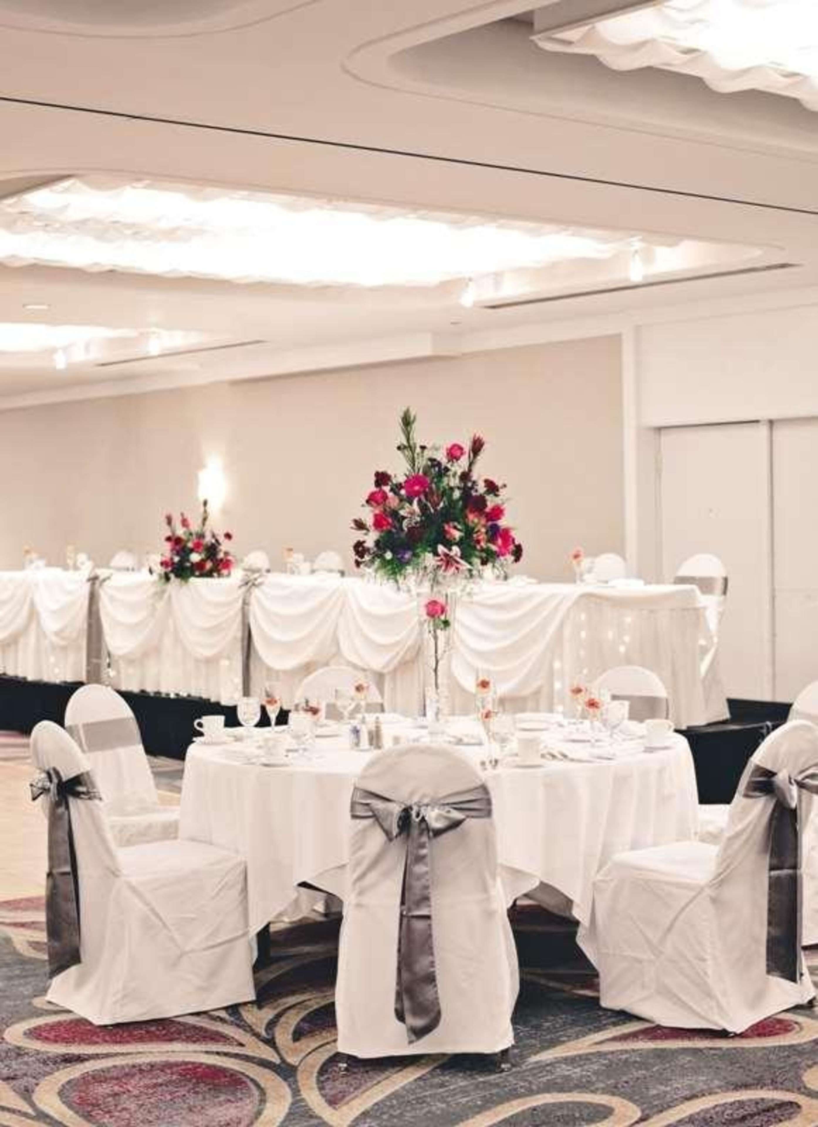 A banquet hall with round tables, white tablecloths, and chairs with gray sashes.