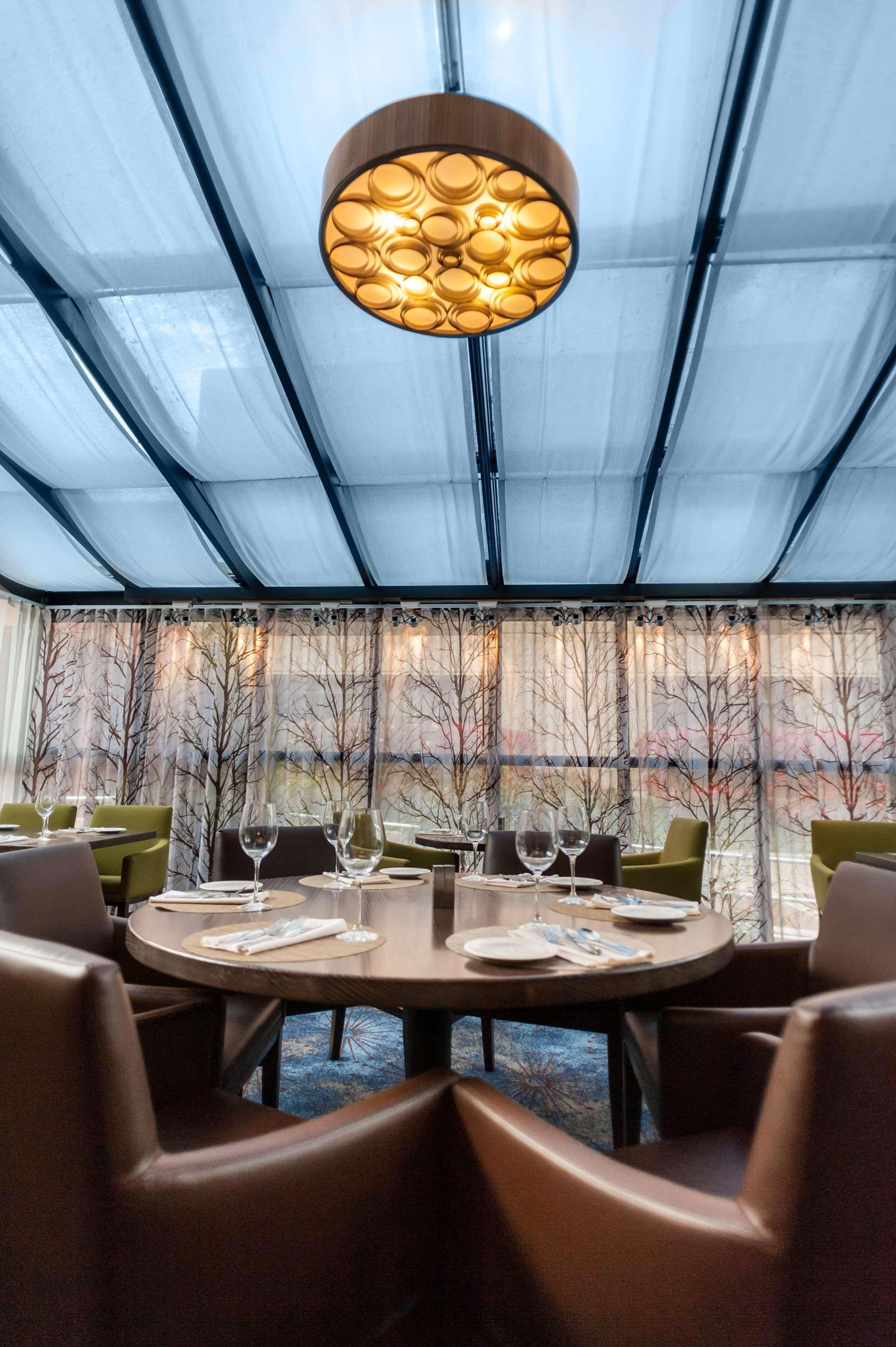 A restaurant with a round table, chairs, and a unique overhead light fixture.