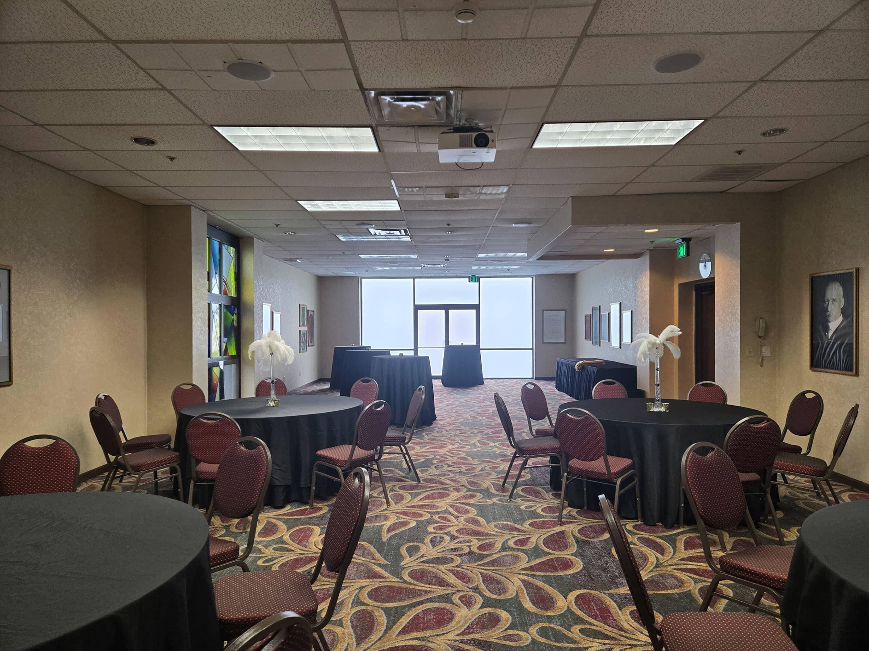 Une salle de conférence équipée de tables et de chaises, d’un projecteur et d’une grande fenêtre.
