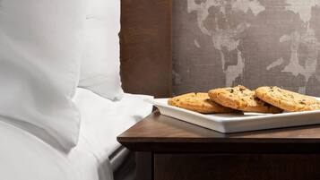 Uma cama com lençóis brancos, um criado-mudo de madeira com um prato de biscoitos e um mapa-múndi na parede.