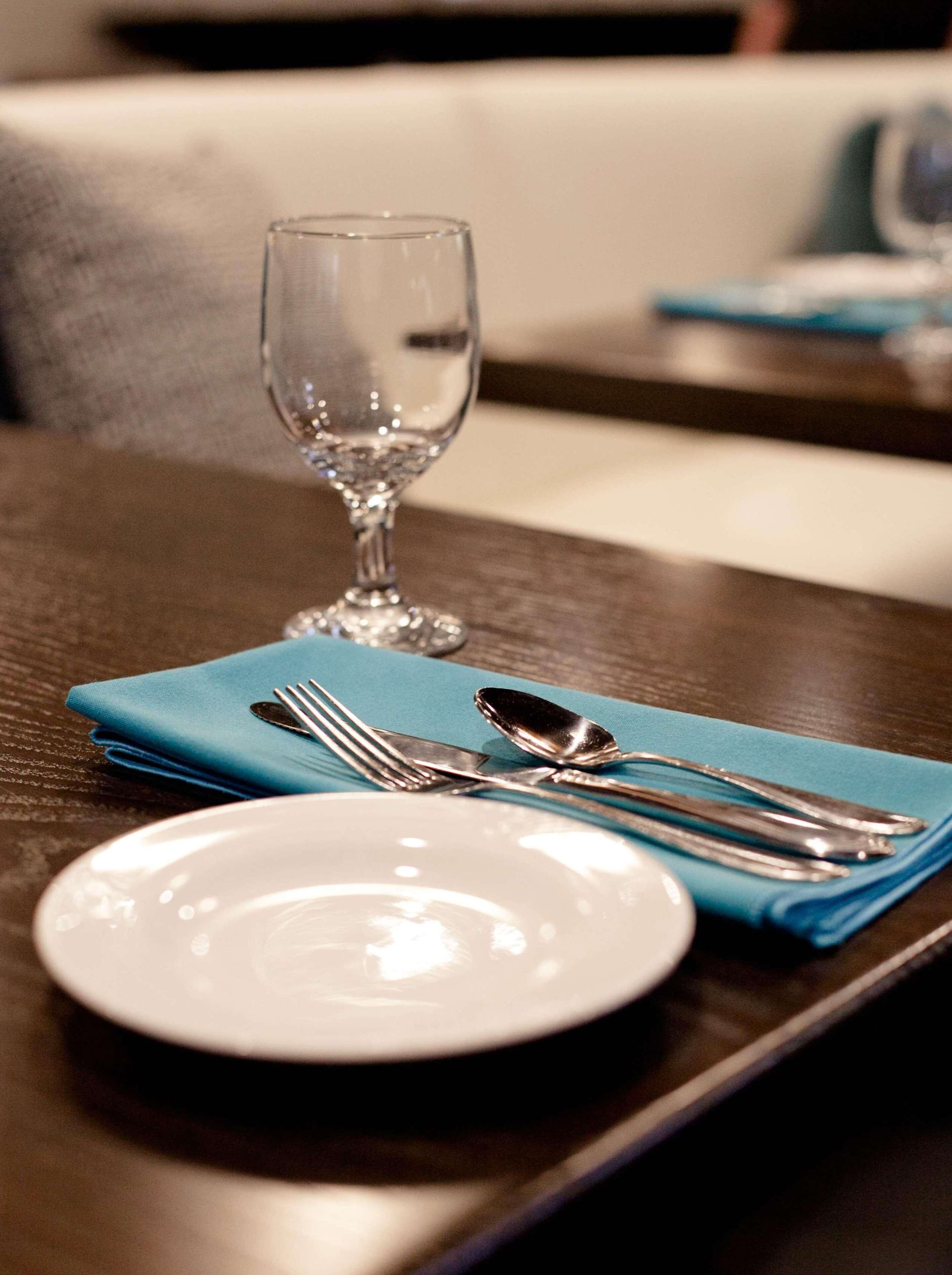 Een eettafel met een wit bord, een blauwe servet en bestek.