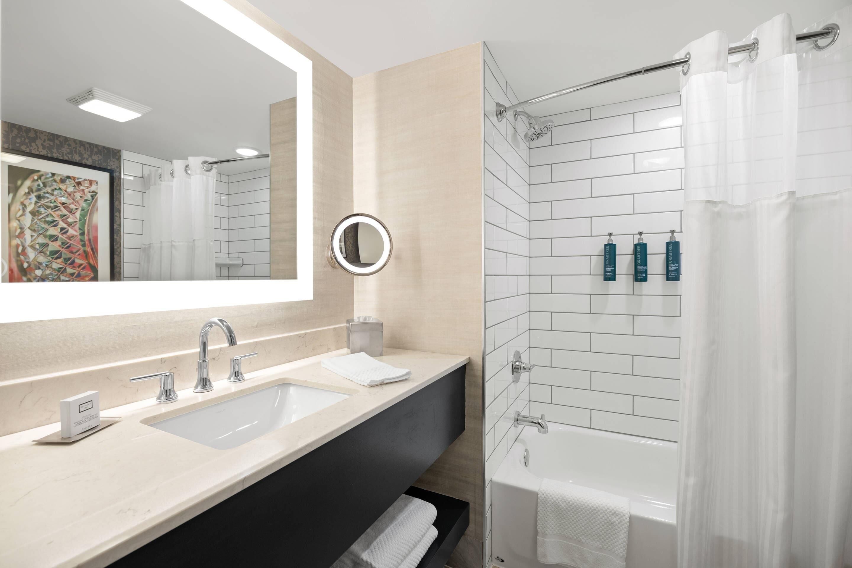 A modern bathroom with a large mirror, two sinks, a bathtub, and a shower curtain.
