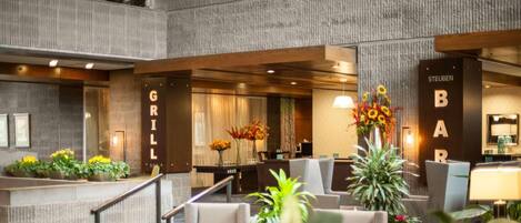 A modern hotel lobby with a reception desk, seating area, and a bar.