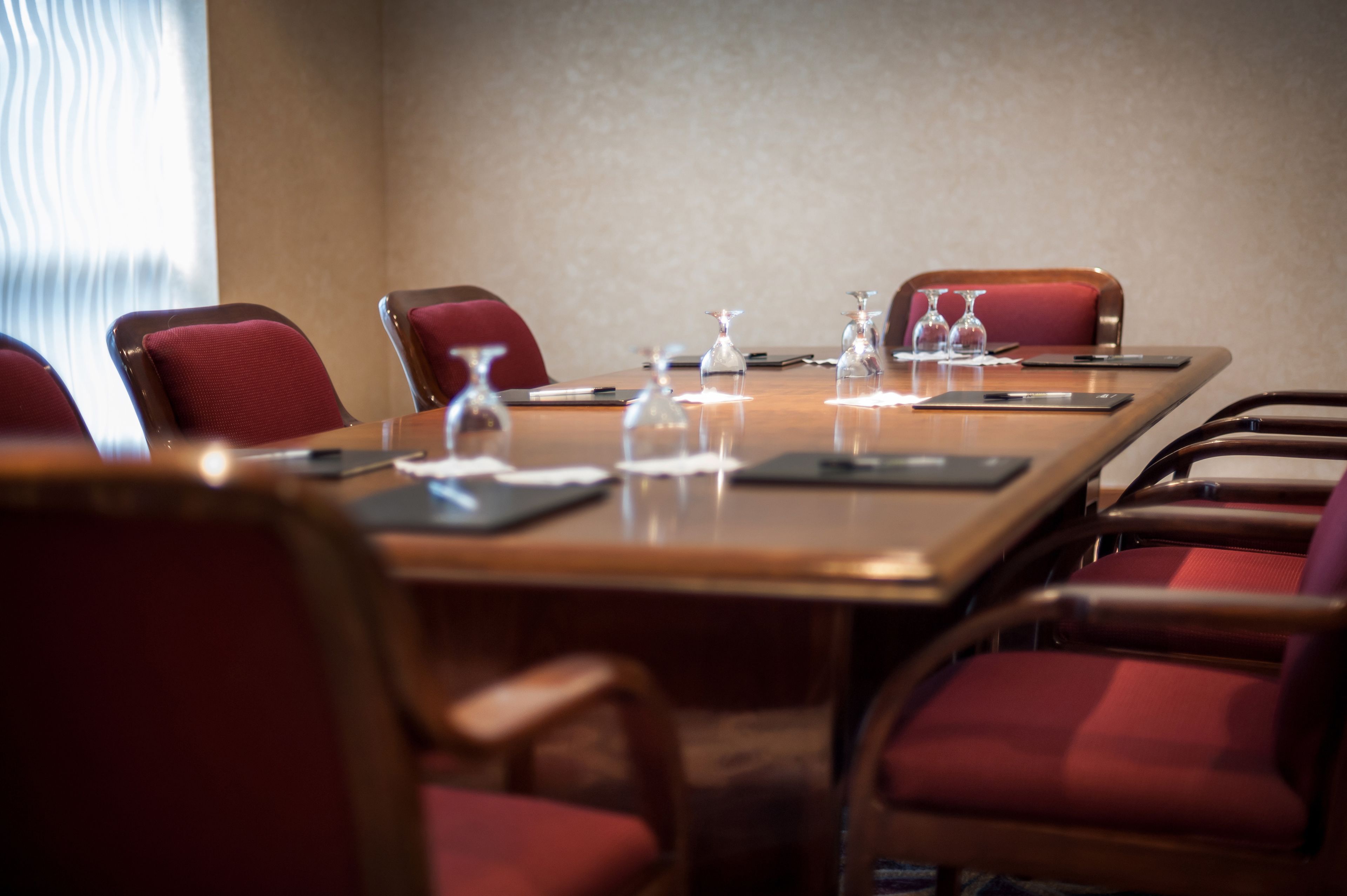 A conference room with a long table, red chairs, and glassware on the table.