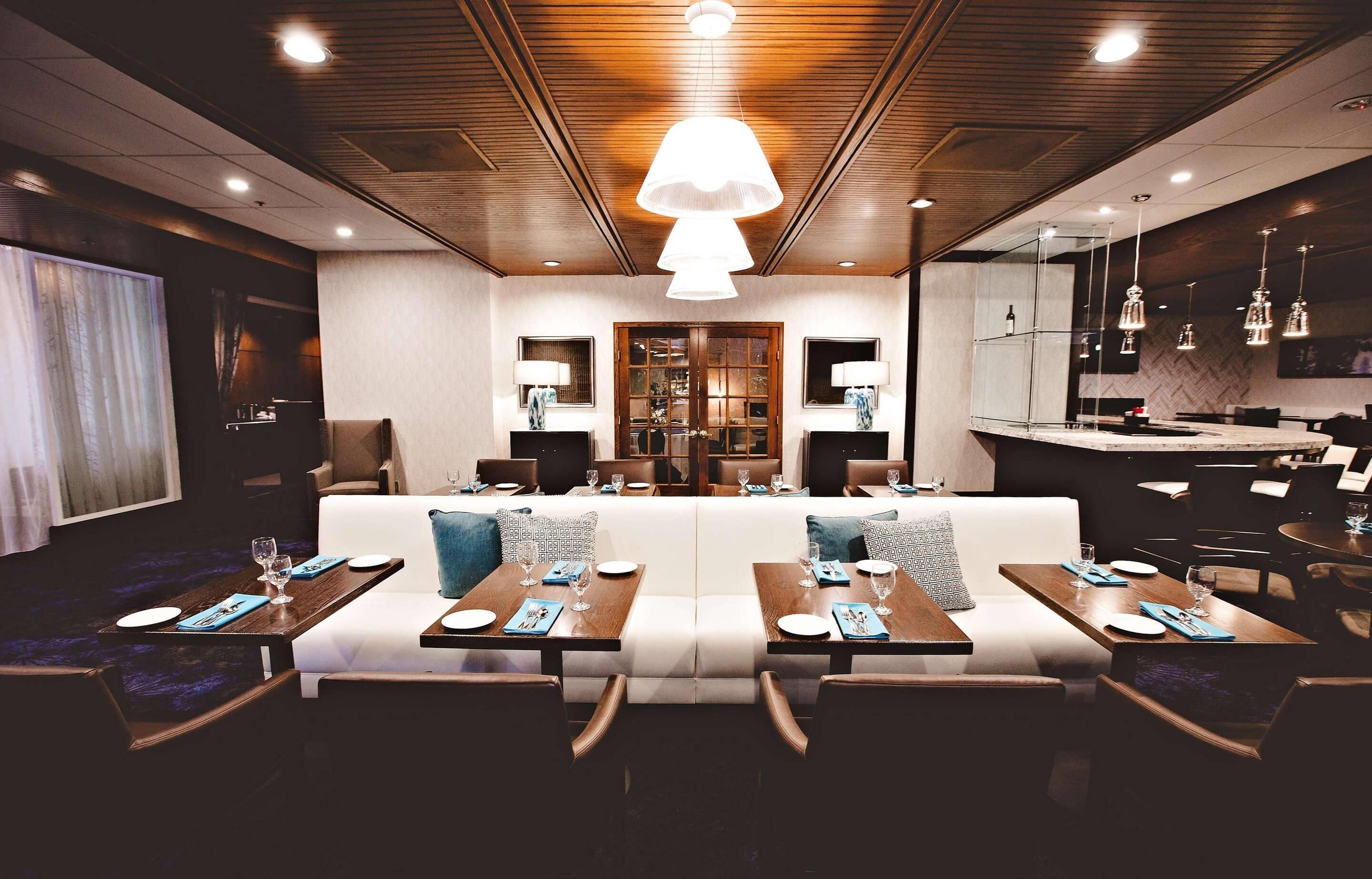 A modern dining area with a central seating arrangement, overhead lighting, and a bar area.