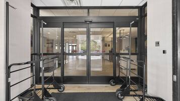 Entrada de hotel con puerta de cristal, felpudo negro y un carrito.