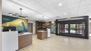 A modern reception area with a wooden reception desk, a glass door entrance, and a cityscape mural on the wall. - La Quinta Inn & Suites by Wyndham Nashville Airport/Opryland (Nashville)