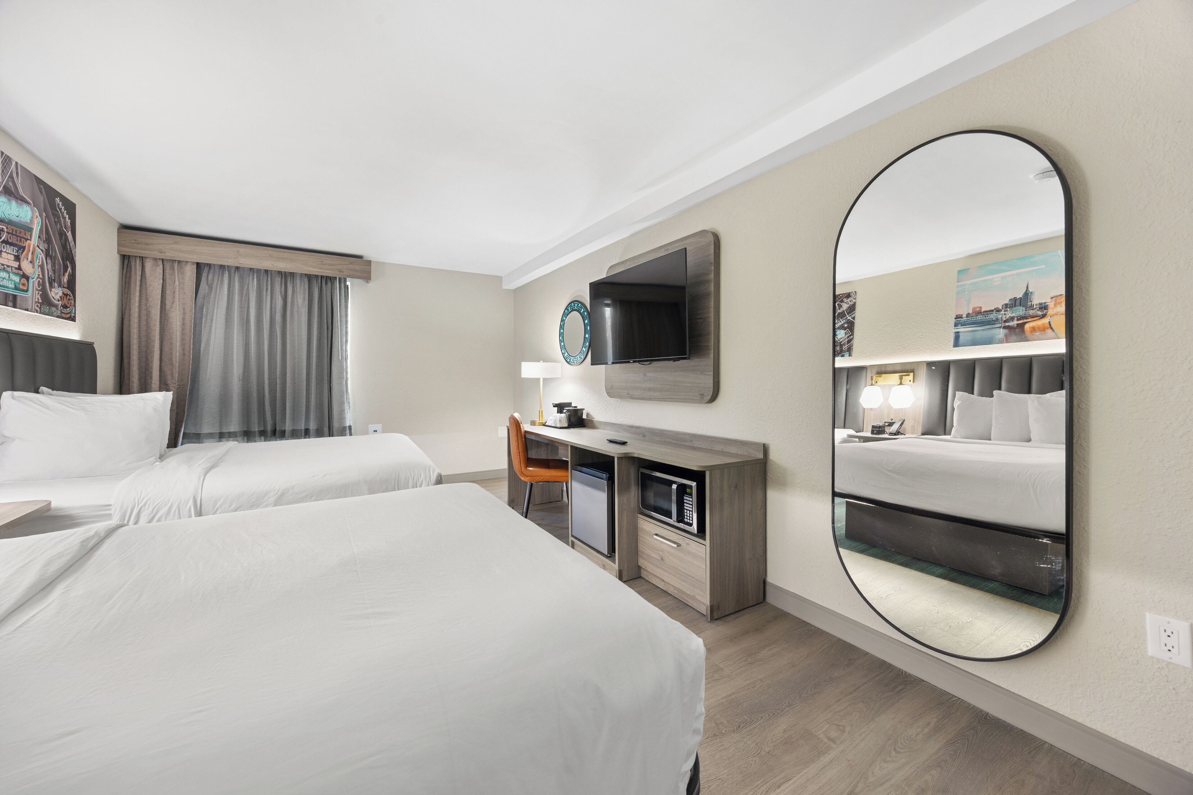 Une chambre d’hôtel avec deux lits, un bureau équipé d’un micro-ondes, une télévision et un grand miroir.