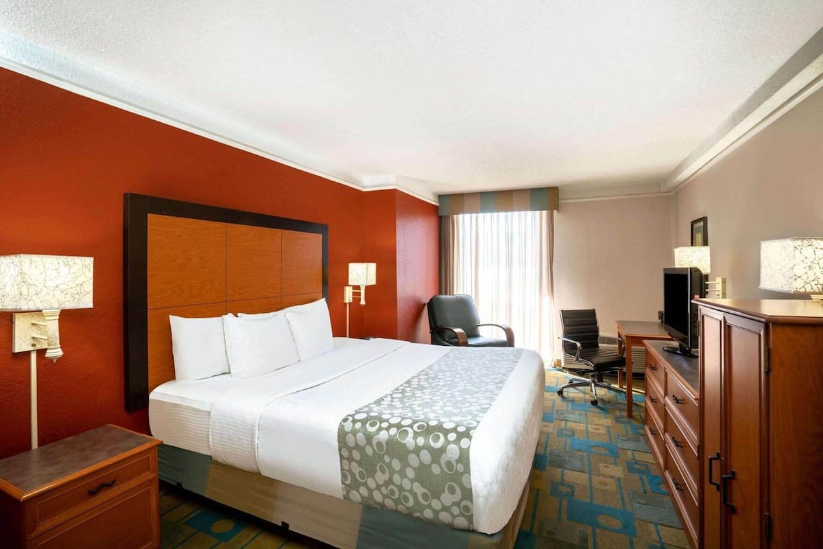 Quarto de hotel com uma cama grande, uma mesa com televisão, uma cadeira e um armário.
