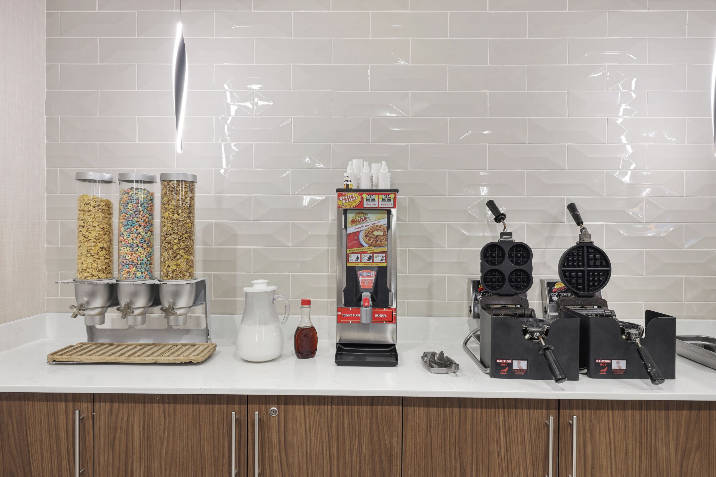 A kitchen counter with waffle makers, a waffle dispenser, and a waffle iron.