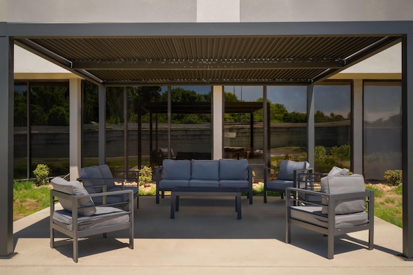 An outdoor seating area with a pergola, modern furniture, and large windows offering views of the landscape.