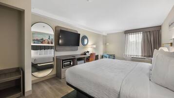 Una habitación de hotel con una cama grande, un televisor de pantalla plana, un escritorio con silla, un espejo redondo y una ventana con cortinas.