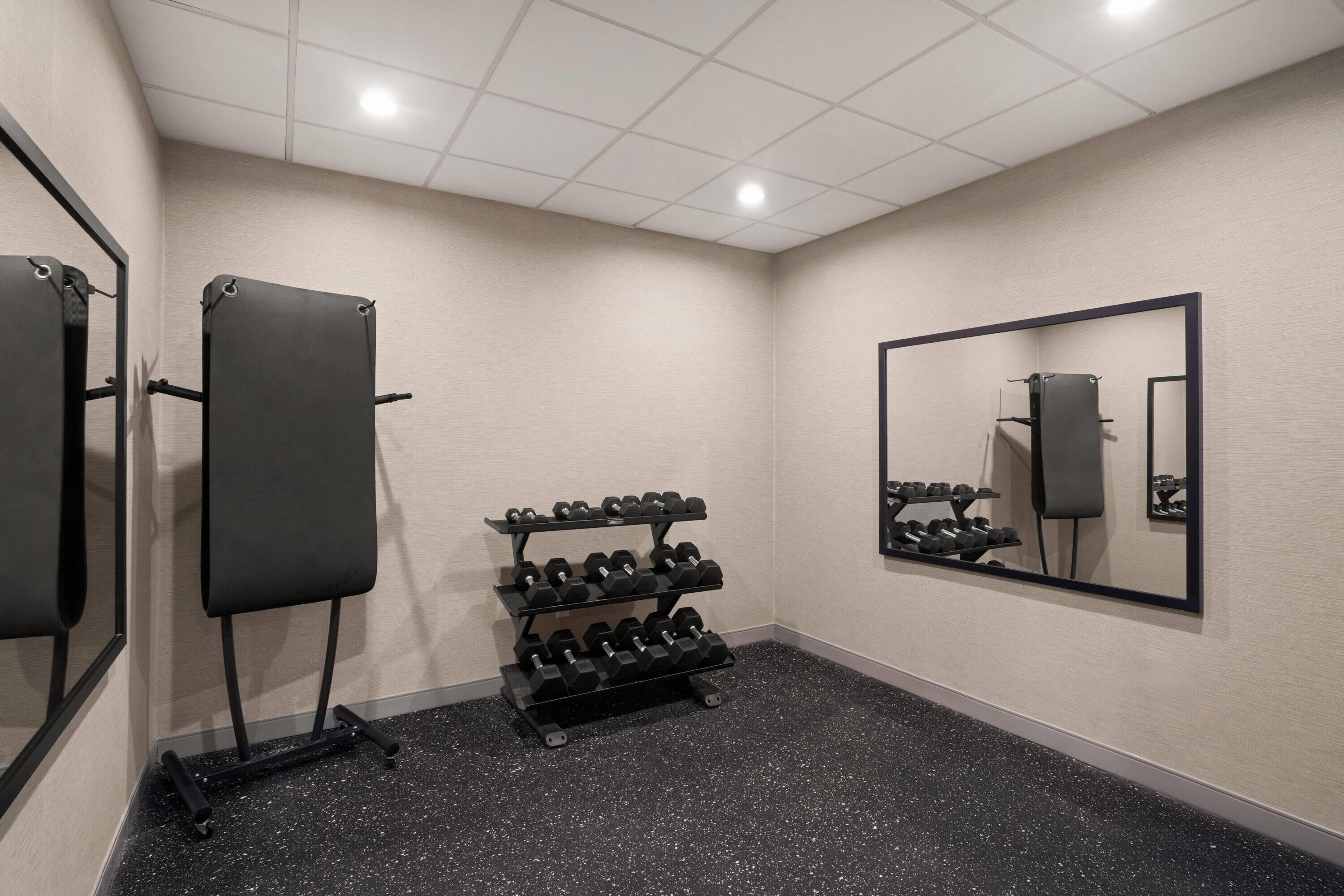 A gym with a mirrored wall, a dumbbell rack, and a black floor.