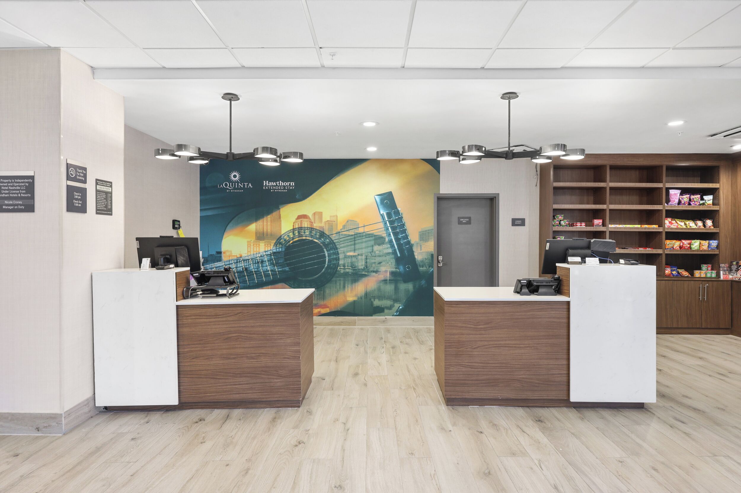 A hotel reception area with two reception desks, a large mural, and a snack shelf.
