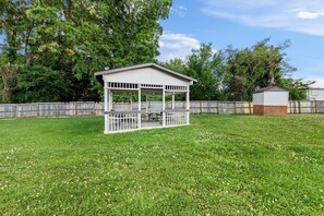 A covered outdoor area with a picnic table, surrounded by a wooden fence and trees. - Super 8 by Wyndham Gaffney (Gaffney)