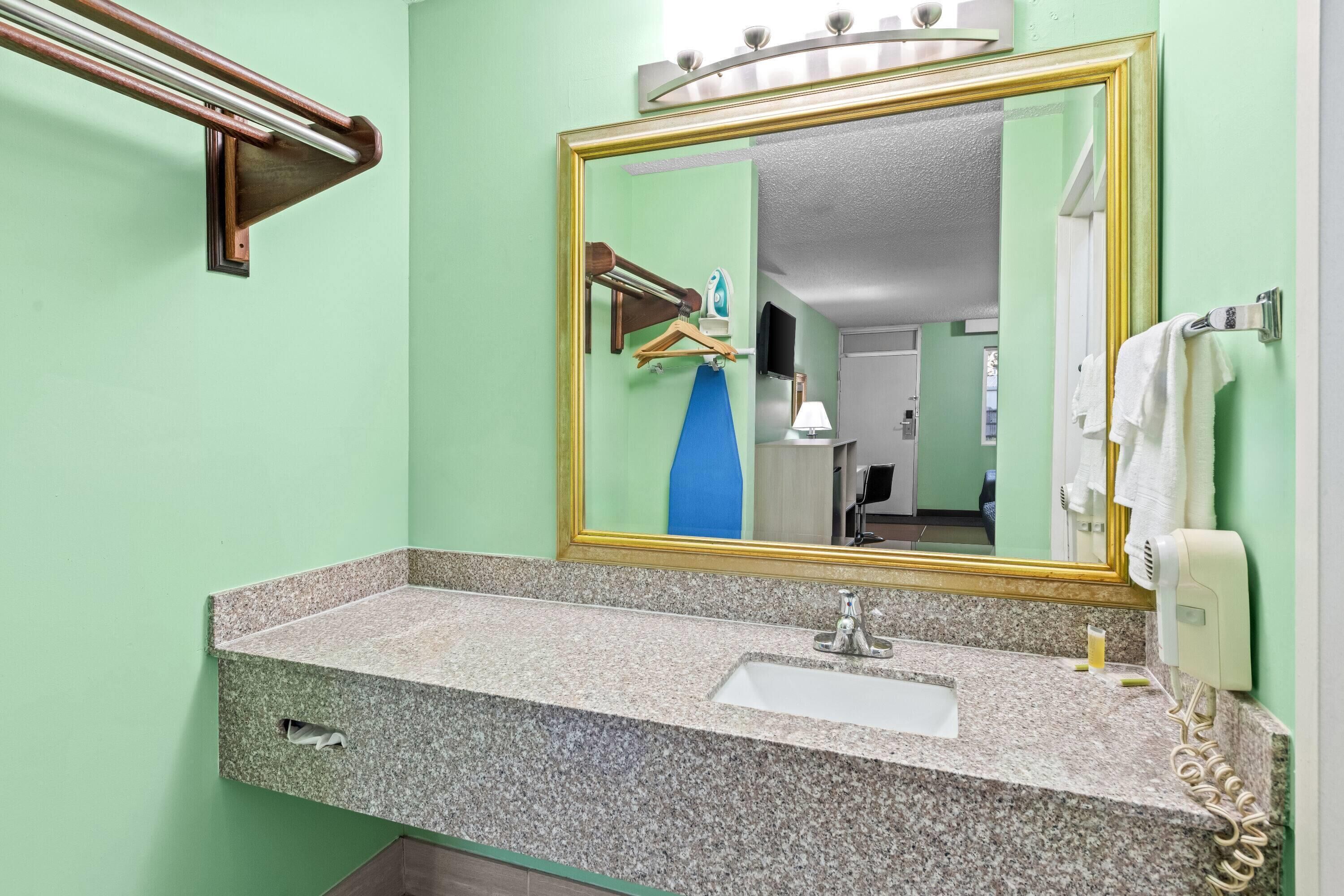 Un baño con lavabo de encimera de granito, espejo con marco dorado, toallero y secador de pelo.