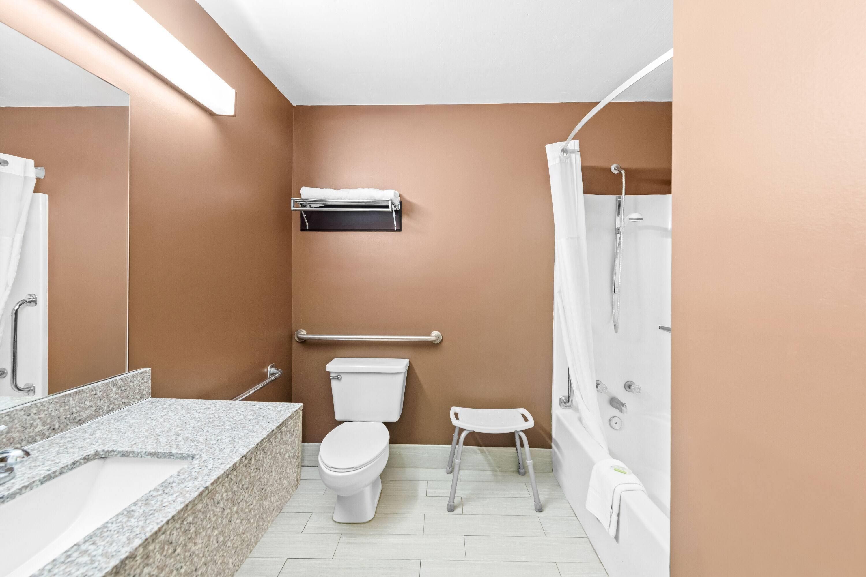A bathroom with a toilet, sink, shower, and a small step stool.