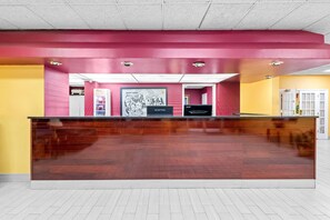 A reception desk with a wooden finish, pink and yellow walls, and a white door in the background. - Super 8 by Wyndham Gaffney (Gaffney)