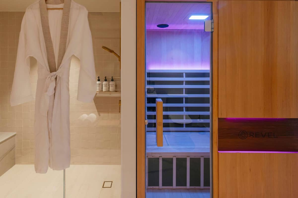 A modern bathroom with a wooden door, a robe hanging on a rack, and a visible shower area.