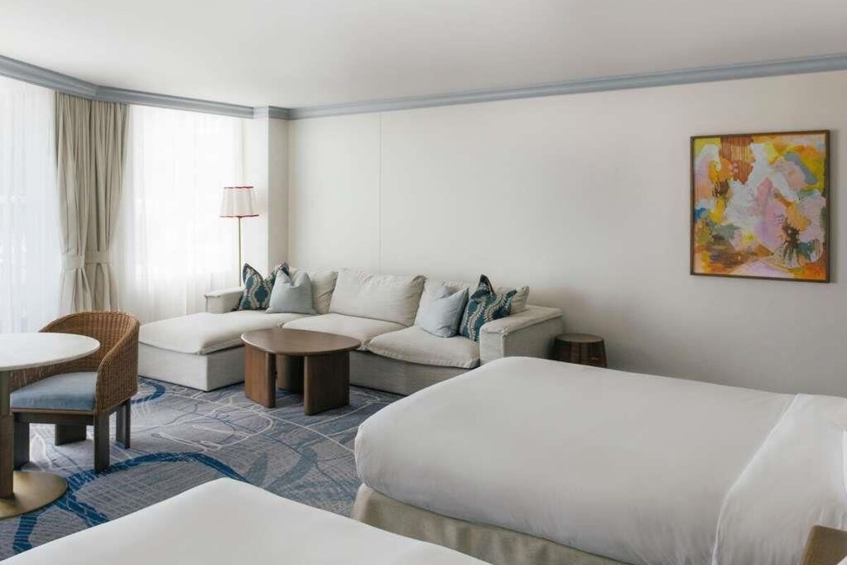 Une chambre d’hôtel avec un canapé, deux lits simples, une table basse ronde, une chaise et une lampe.