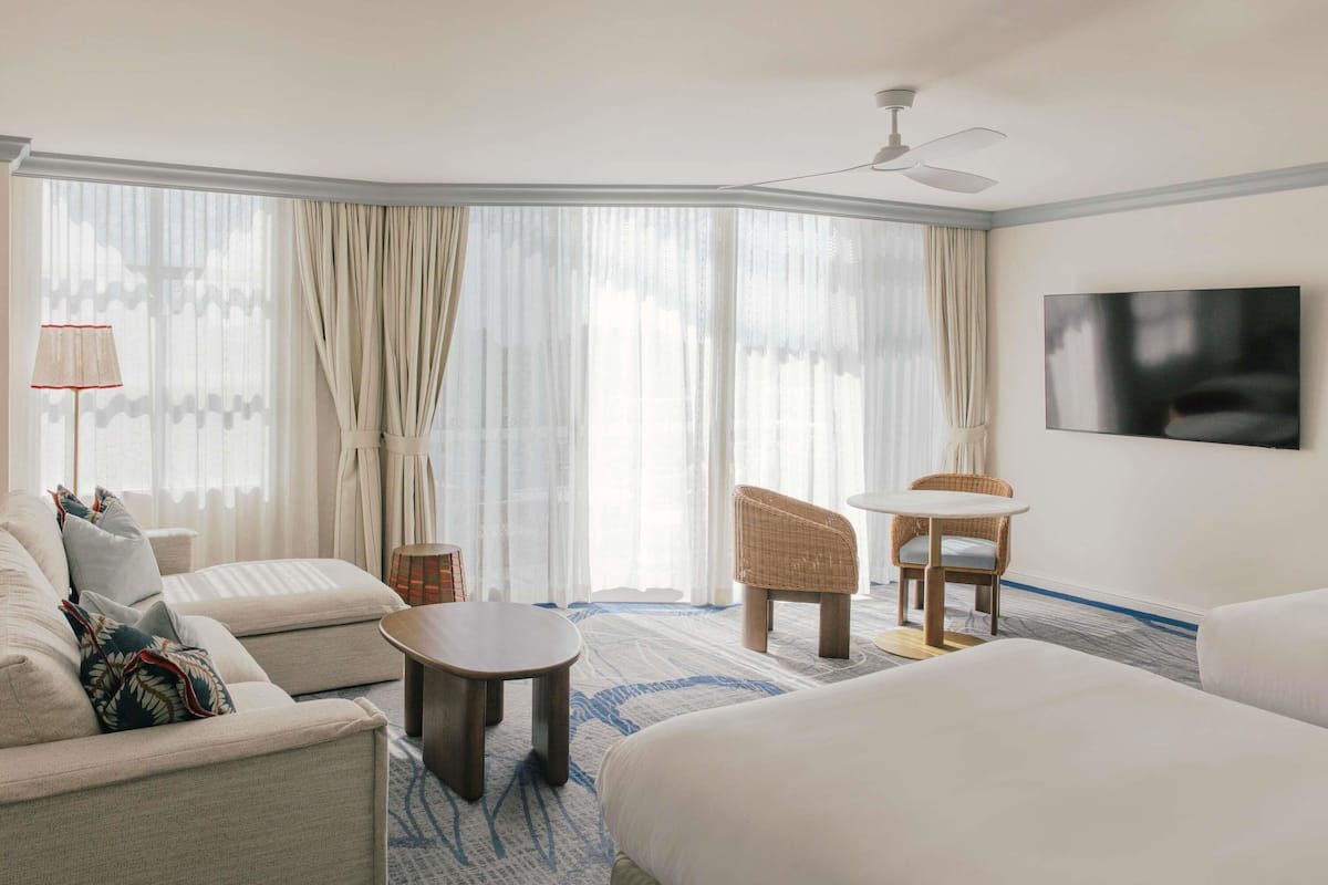 A hotel room with a bed, a sofa, a chair, a small table, and a TV on the wall.