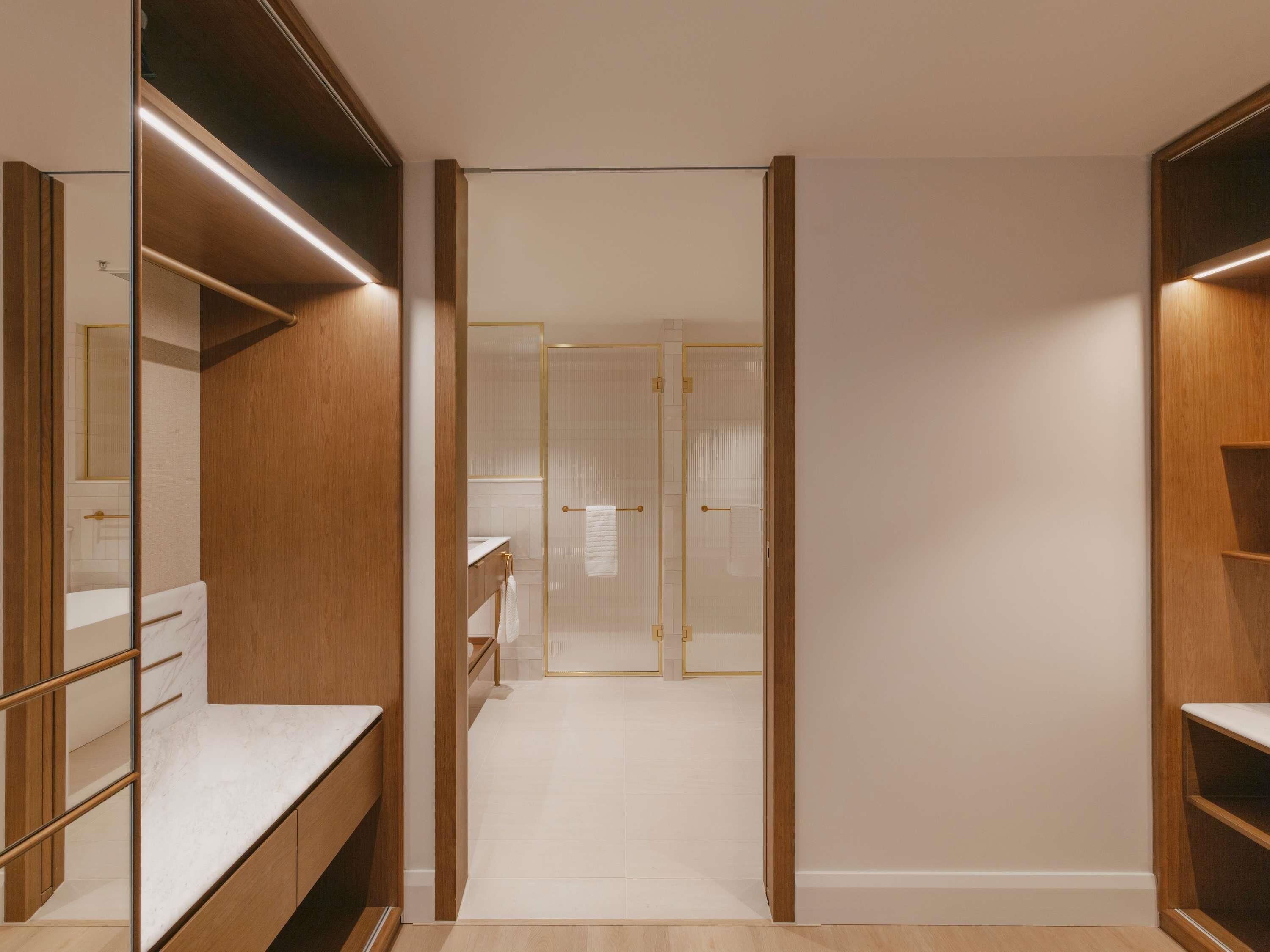 A walk-in closet with mirrored doors, wooden shelving, and a marble countertop.