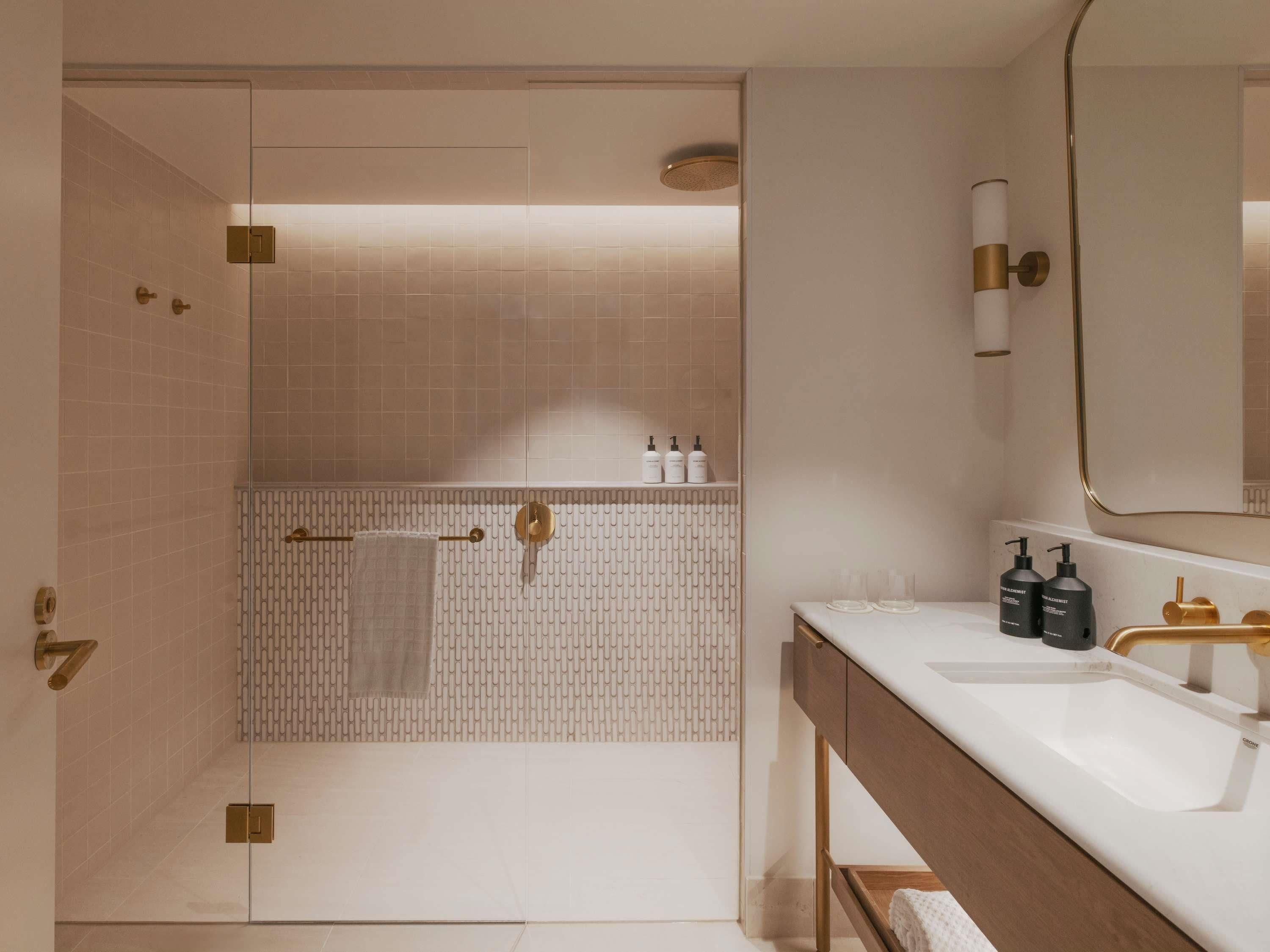 A modern bathroom with a glass shower enclosure, a vanity with a gold faucet, and a mirror above the sink.