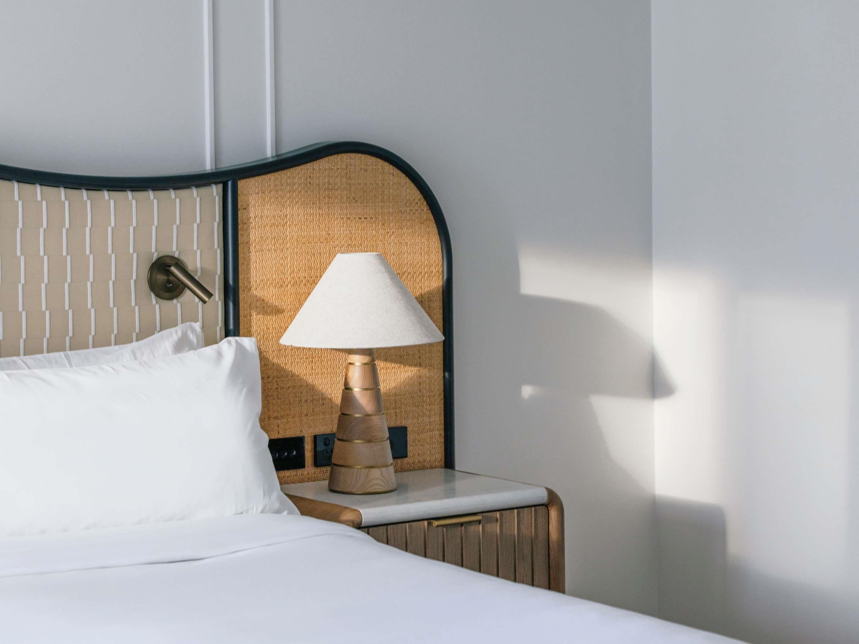A neatly made bed with white linens, a wooden nightstand with a lamp, and a textured wall behind the headboard.