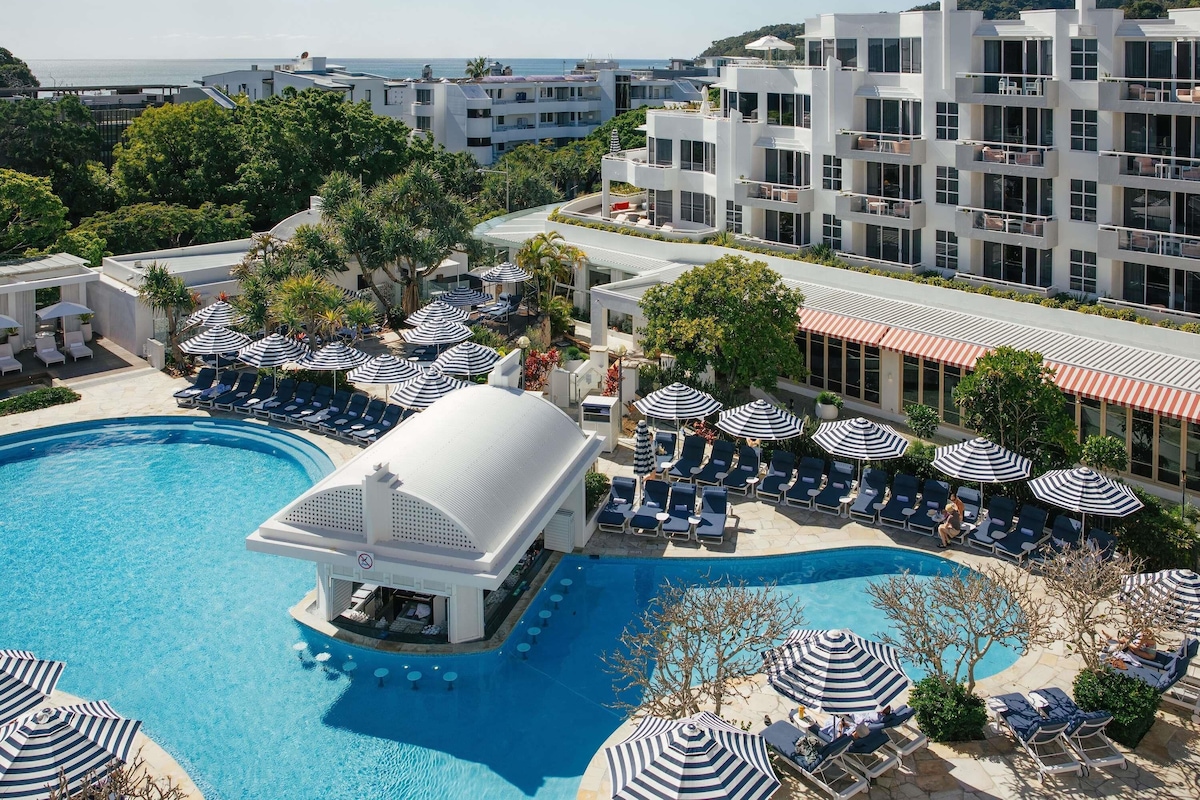 A resort with a swimming pool, lounge chairs, umbrellas, and a view of the sea.