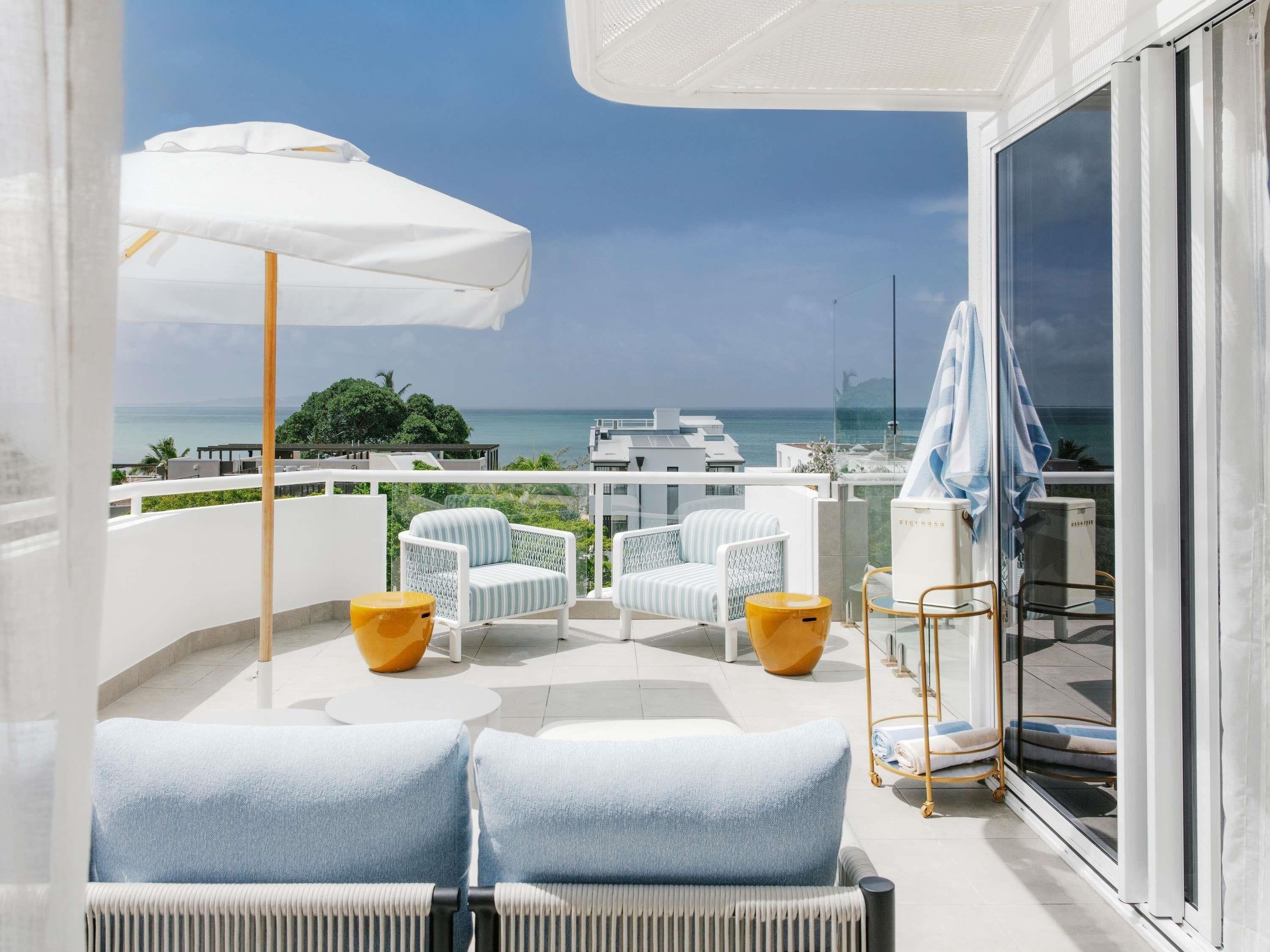 A balcony with a white sofa, two chairs, a table, and a sun umbrella.