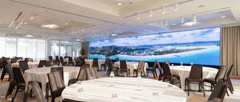 A conference room with round tables, chairs, and a large screen displaying a scenic view.