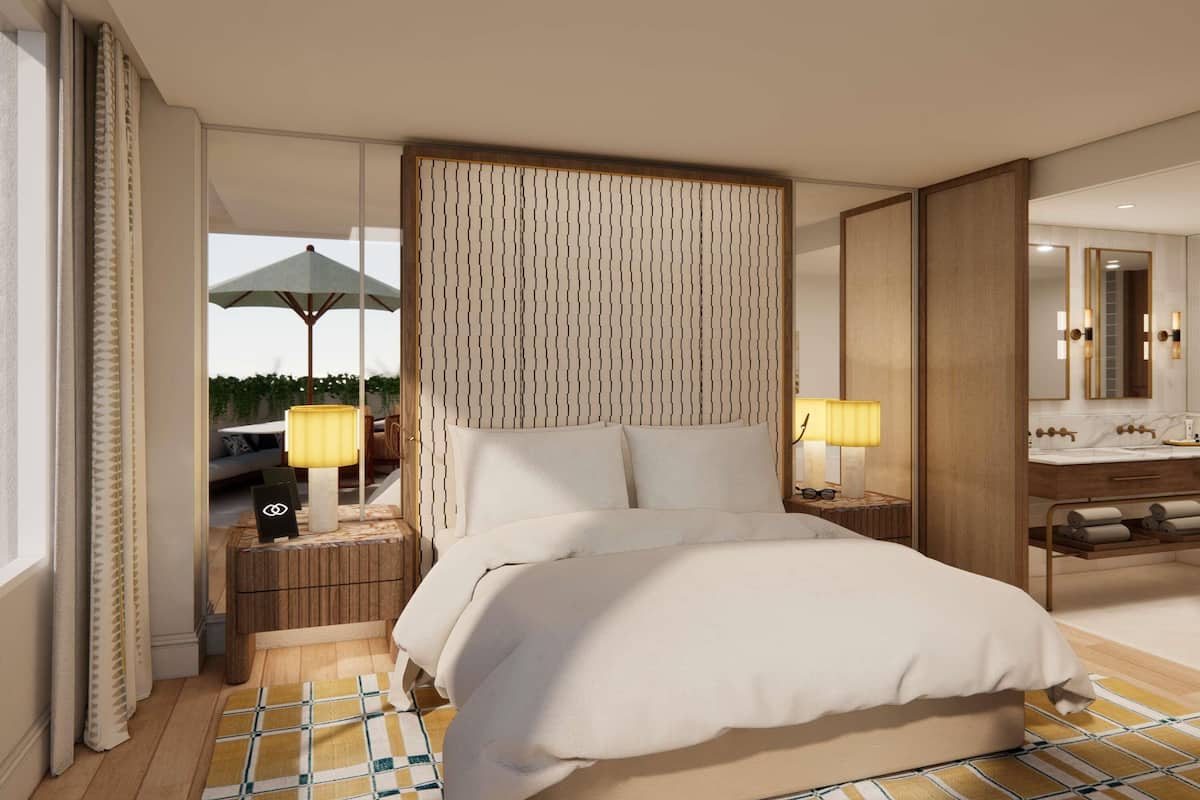 A hotel room with a large bed, a wooden headboard, a bathroom with a mirror and sink, and a view of the outdoors.