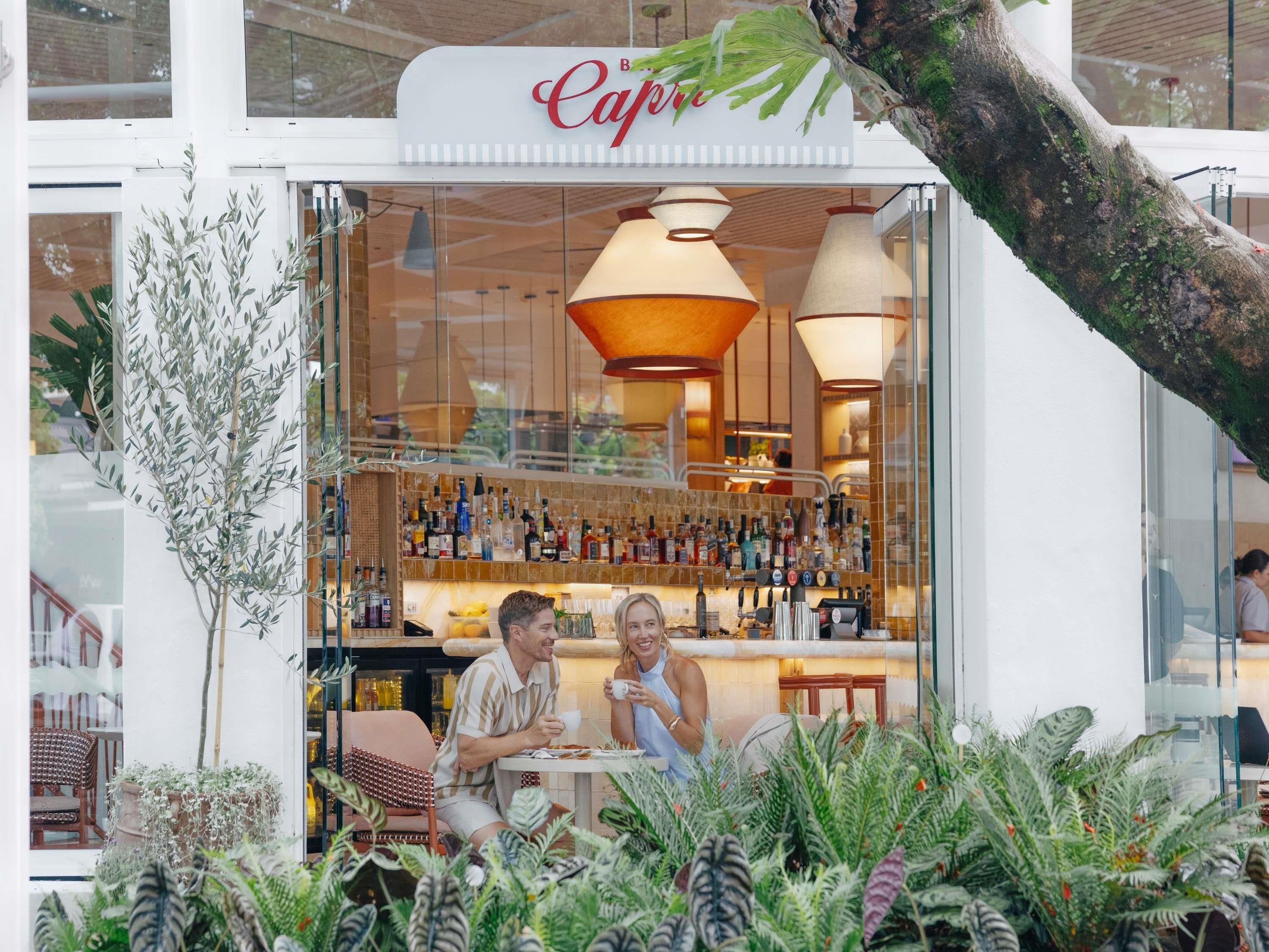 En café med facade af glas, et barområde med flasker og indeplanter.