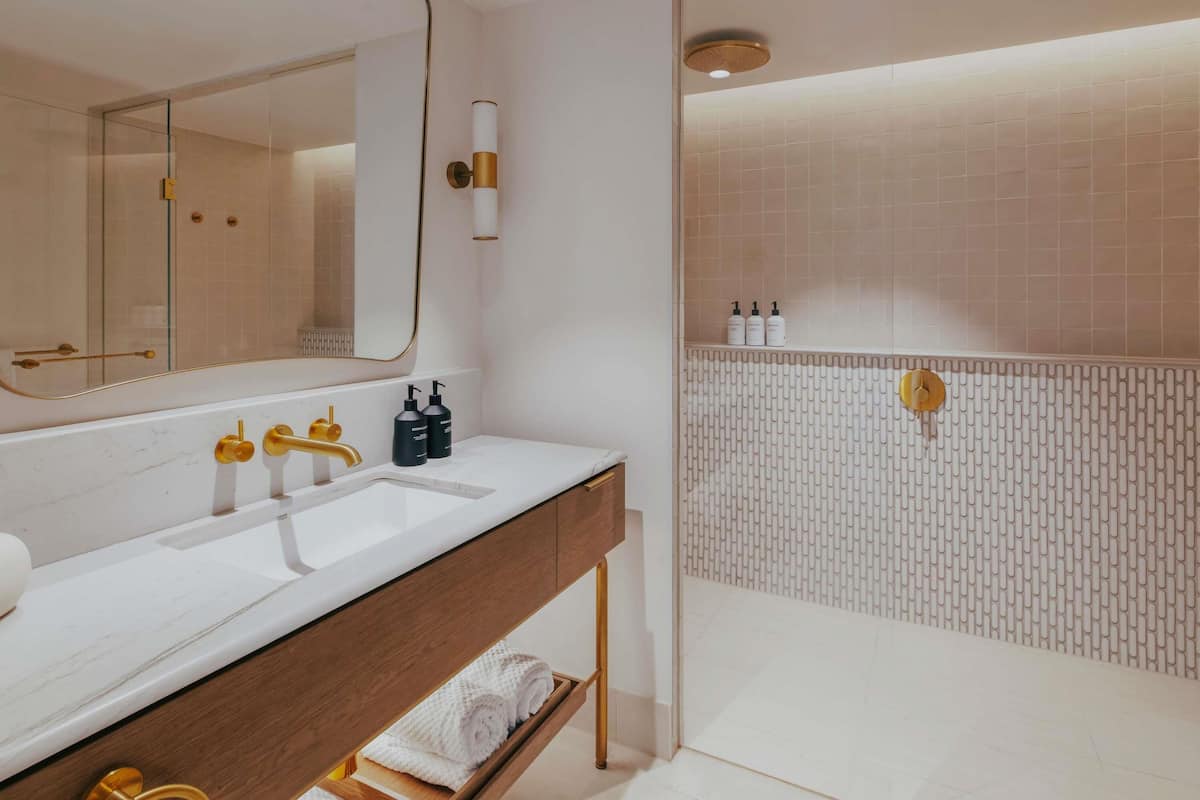 A modern bathroom with a dual sink vanity, a large mirror, and a walk-in shower with a patterned tile wall.