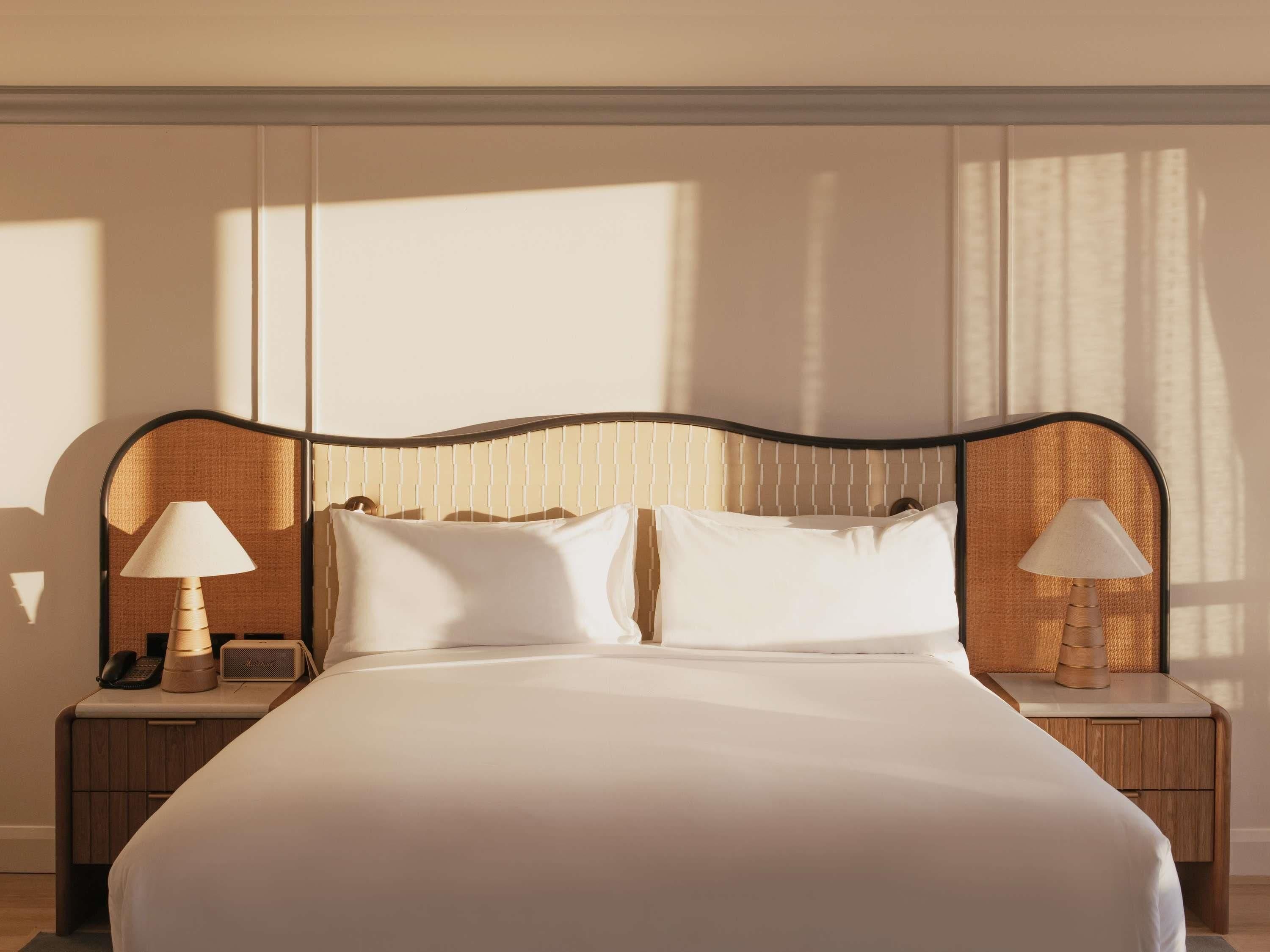 A neatly made bed with a headboard, two bedside tables with lamps, and a telephone on one of the tables.