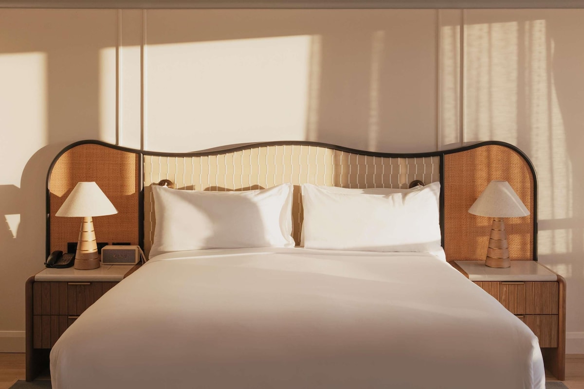A neatly made bed with a headboard, two bedside tables with lamps, and a telephone on one of the tables.