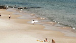 A beach with people walking and sitting, a surfboard, and waves approaching the shore.
