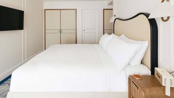 A hotel room with a large bed, a bedside table with a lamp, a flat-screen TV mounted on the wall, and a wardrobe with a mirror.
