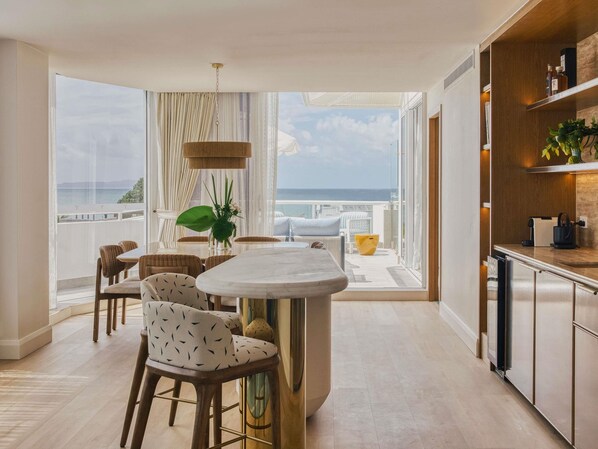 A modern kitchen with a central island, a dining area with wicker chairs, and a view of the sea.
