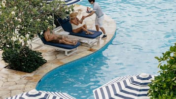 Zona de piscina con sillones de descanso y sombrillas a rayas.