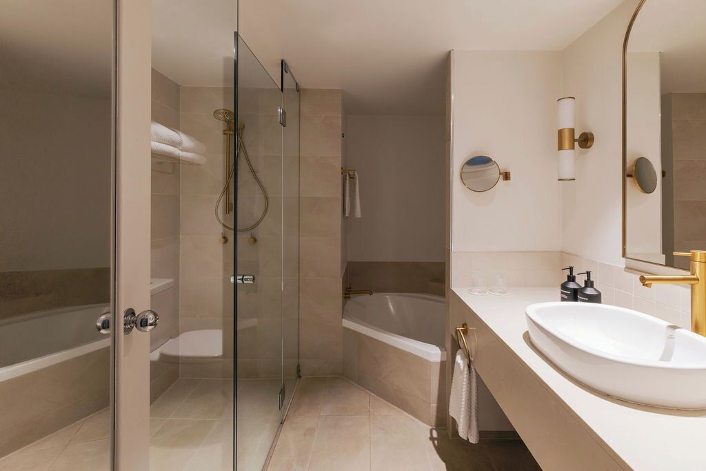 A modern bathroom with a glass-enclosed shower, a freestanding bathtub, and a white sink with gold fixtures.