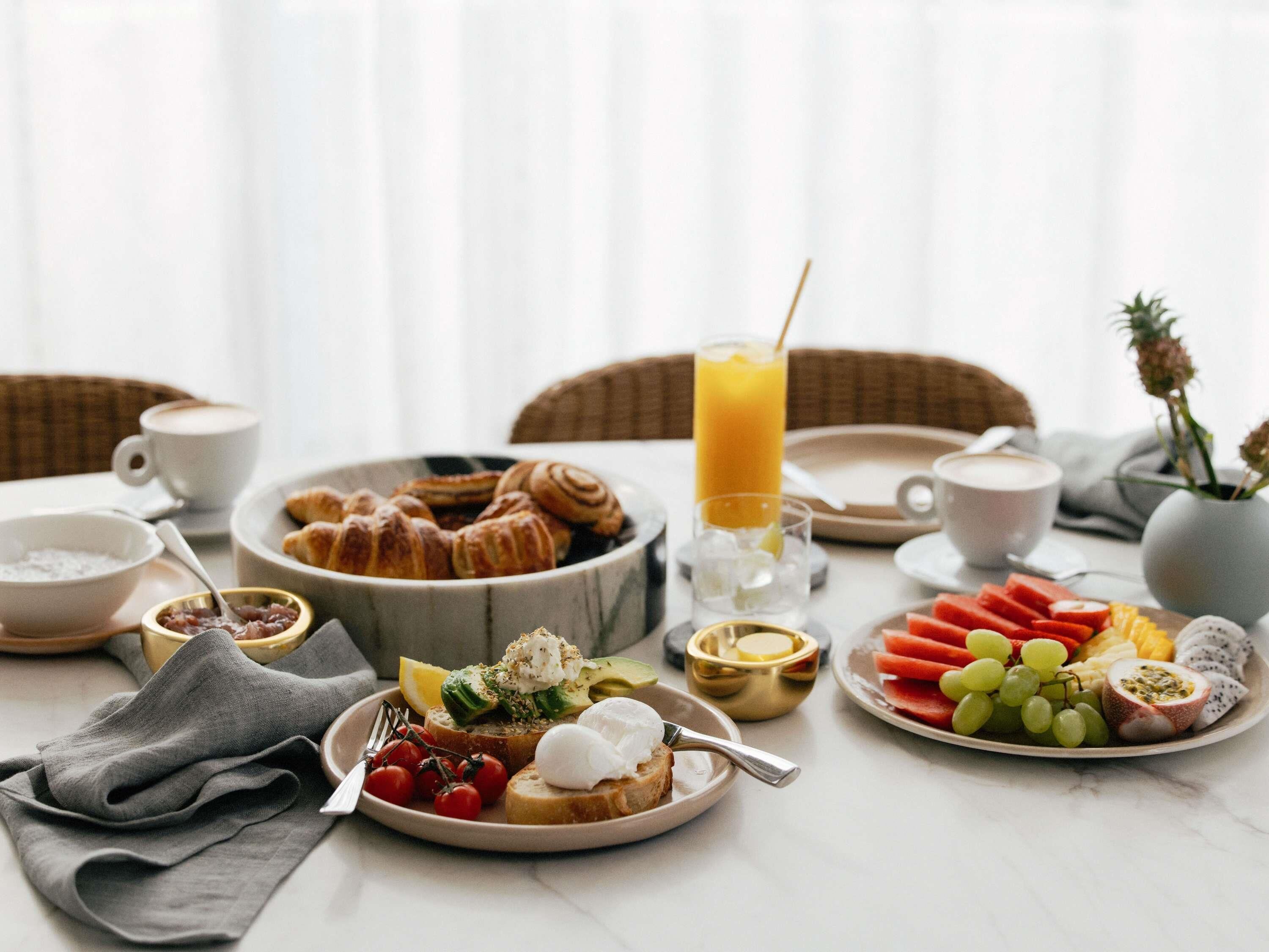 A breakfast setting with croissants, toast with toppings, fruit, and a glass of orange juice.