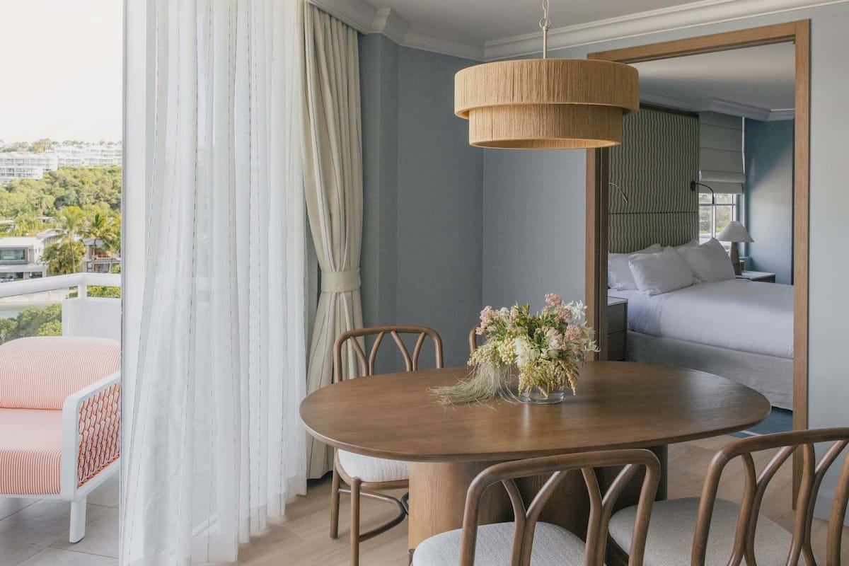 A hotel room with a dining table, chairs, a bed, and a view of the outside.