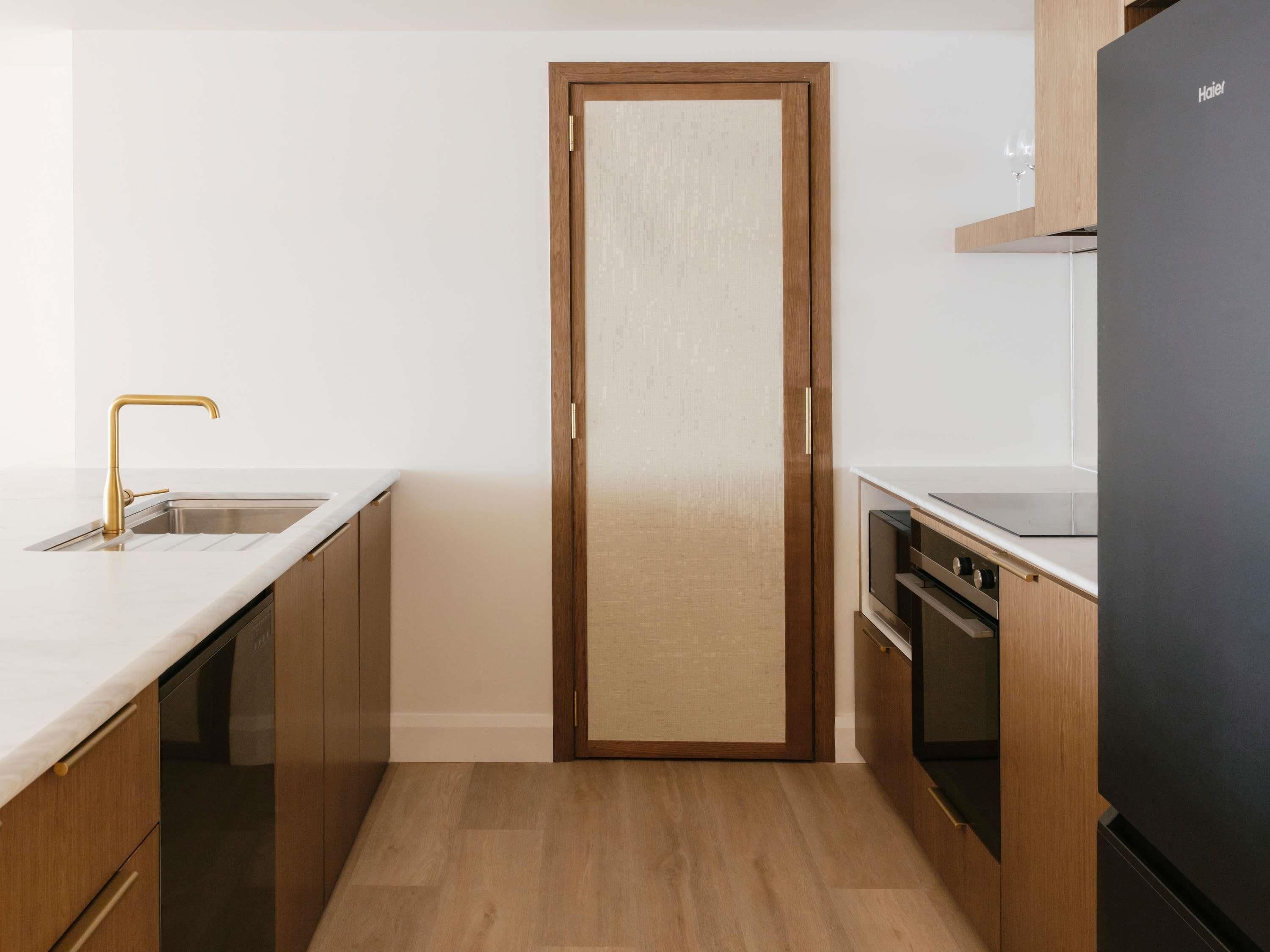 A compact kitchen with a wooden door, a stainless steel sink, and a black refrigerator.