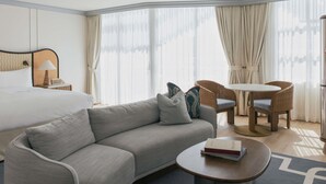 Habitación de hotel con cama, sofá, mesa redonda, silla, mesita pequeña y ventilador de techo.