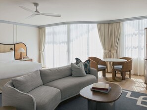A hotel room with a bed, a sofa, a round coffee table, a chair, a small table, and a ceiling fan. - Elysium Noosa Resort - MGallery Collection (Noosa Heads)